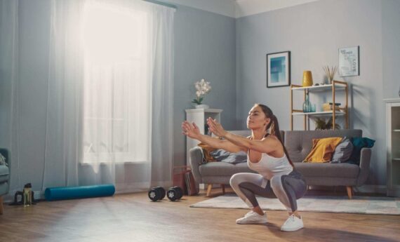 Una mujer haciendo sentadillas en el salón de su casa, representando el entrenamiento en casa