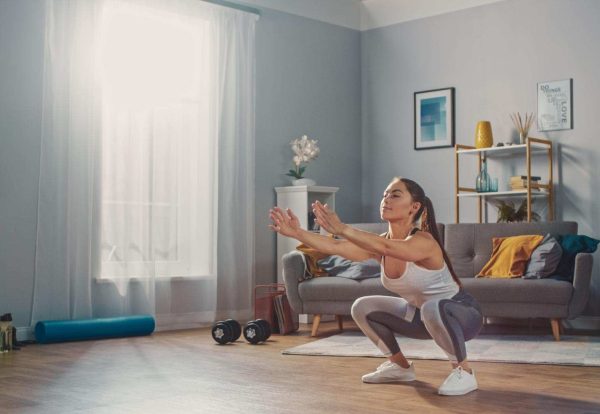 mujer-entrenamiento-en-casa Una mujer haciendo sentadillas en el salón de su casa, representando el entrenamiento en casa