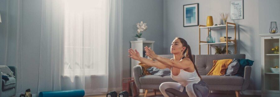 Una mujer haciendo sentadillas en el salón de su casa, representando el entrenamiento en casa