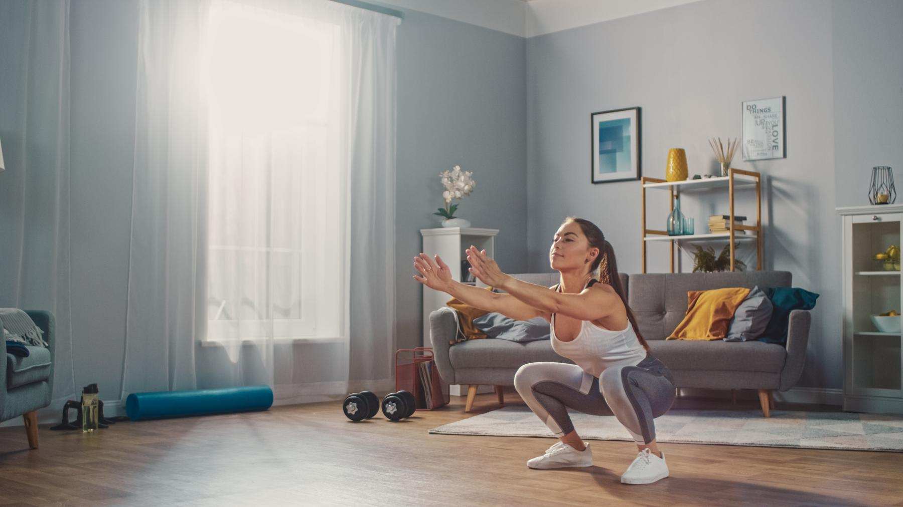 Una mujer haciendo sentadillas en el salón de su casa, representando el entrenamiento en casa