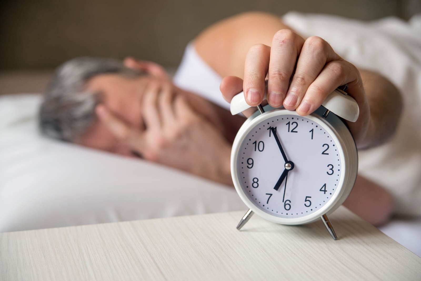 Persona con la mano en la cabeza, expresando cansancio y ansiedad post-vacaciones, con un despertador en primer plano.