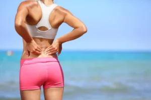 Mujer de espaldas frotándose la zona lumbar por dolor en la espalda.
