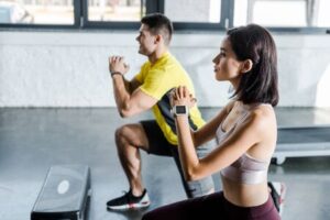 Pareja realizando sentadillas con un step en un gimnasio, demostrando un entrenamiento personalizado y funcional.